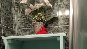 Un baño con pared revestida de mármol, cabina de ducha de vidrio y un estante con toallas dobladas.