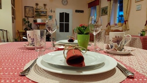 Una mesa de comedor dispuesta con platos, vasos y cubiertos, con un centro de mesa decorativo y un reloj en la pared.