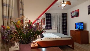 Un dormitorio con una cama, un aparador de madera, un televisor y un ventilador de techo.
