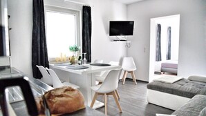 Un apartament modern amb zona de menjador, saló i televisió penjada a la paret.