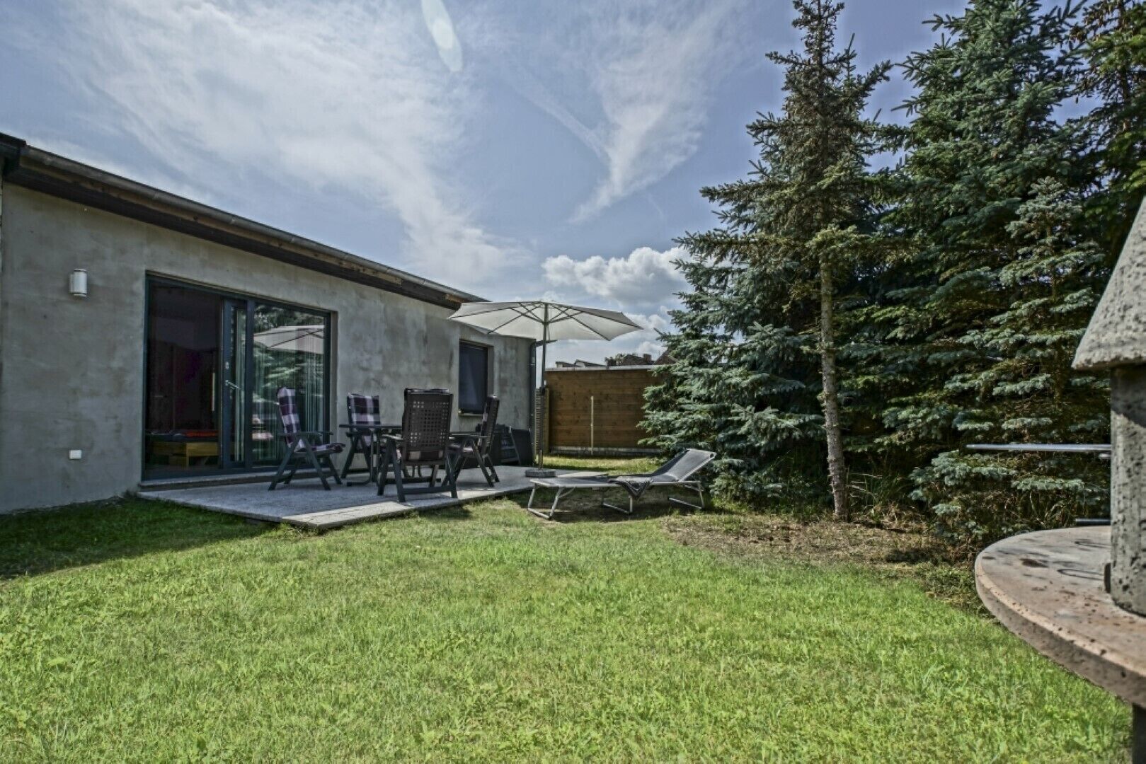 A modern house with a patio, outdoor furniture, and a large tree.