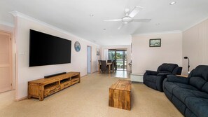 A spacious living room with a flat-screen TV, wooden entertainment unit, and a dark sofa. - Dunworkin - Relax by the river (Dunbogan)