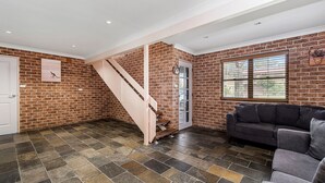 Una habitación con pared de ladrillo, una escalera, un sofá gris y una ventana con persianas.