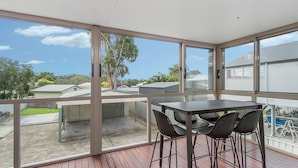 Un balcón con mesa y sillas, ventanas amplias y vistas a casas vecinas.