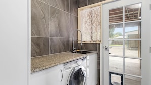 Un área de lavandería con lavadora, un lavamanos y una ventana con cortinas de encaje.