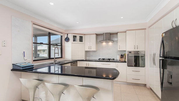 Una cocina moderna con una isla central, armarios blancos, electrodomésticos de acero inoxidable y un ventanal con vistas al exterior.