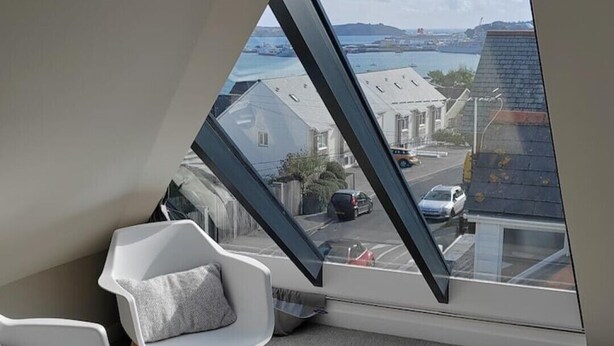 Una habitación con techo inclinado y vistas a un barrio residencial.