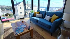 Un salón moderno con un sofá azul, una mesa de centro con revistas y grandes ventanales con vistas al mar y edificios.