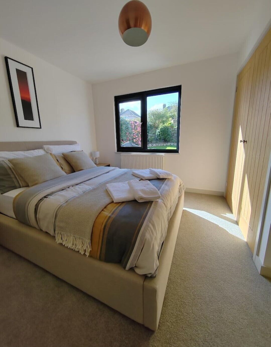 Quarto moderno com uma cama grande, uma janela com vista para vegetação e um radiador.