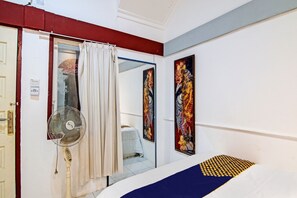 Een hotelkamer met een bed, een ventilator, een spiegel en een deur met een rode omlijsting.