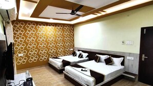 A hotel room with two beds, a ceiling fan, a wall with a geometric pattern, and a desk with a lamp and a power strip. - Diva Pushkar (Pushkar)