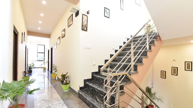 A hallway with a marble floor, a staircase with black steps and a metal railing, and several potted plants. - Diva Pushkar (Pushkar)