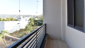A balcony with a metal railing, a window, and a view of buildings and greenery in the distance. - Diva Pushkar (Pushkar)