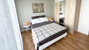 A bedroom with a large bed, a bedside table with a lamp, a hanging artwork, and a wardrobe with a mirror.