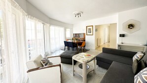 A spacious living room with a sofa, armchair, and a dining table with chairs.