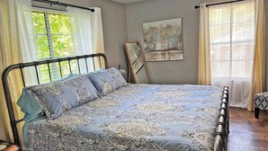 Een slaapkamer met een bed, gordijnen, een schilderij en een plafondventilator.