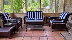 Een overdekt terras met rieten meubels, waaronder een bank en twee fauteuils, en een kleine tafel.