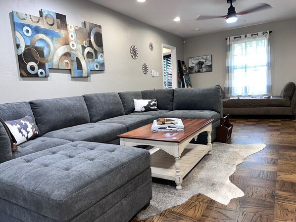Ein Wohnzimmer mit grauem Ecksofa, einem Holztisch und einem weißen, flauschigen Teppich.