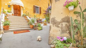 A courtyard with a wooden door, steps, potted plants, and a small statue. - Apartment Minù (Chianciano Terme)