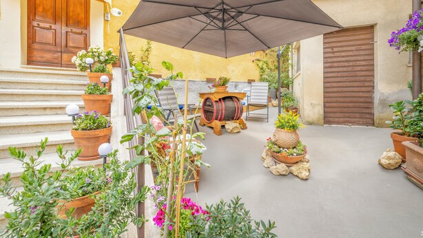 A courtyard with terracotta planters, a wooden barrel, and a large umbrella. - Apartment Minù (Chianciano Terme)