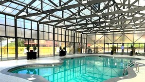 An indoor swimming pool with a glass ceiling, surrounded by a poolside area with seating and potted plants.