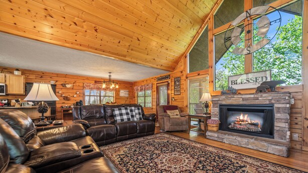A cozy log cabin interior with a fireplace, leather sofas, and a large rug.