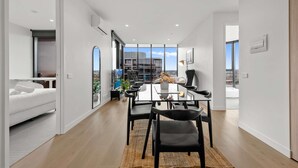 En moderne, åben planløsning med spiseplads, sofa og udsigt til bybilledet gennem store vinduer.
