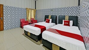 A hotel room with two beds, a red chair, a small table, and patterned wallpaper. - SPOT ON 91376 Hotel Bintang Flores (Cilacap)