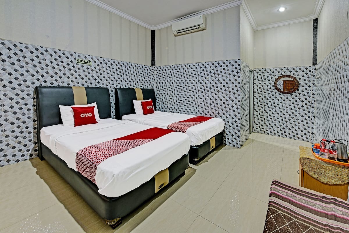 Habitación de hotel con dos camas, una mesita y una bandeja con objetos, y paredes con diseño.