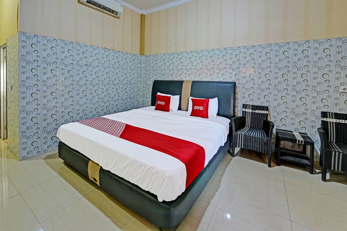 Una cama bien tendida con una colcha roja y blanca, dos almohadas con el logotipo 'OYO' y un cabecero negro.