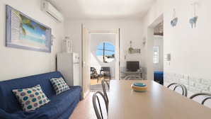 Un salon accueillant avec un canapé bleu, une table à manger et des chaises, et une cuisine visible à travers une porte ouverte.