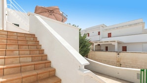Un escalier extérieur menant à une terrasse dotée d’un mur blanc et d’un toit beige.
