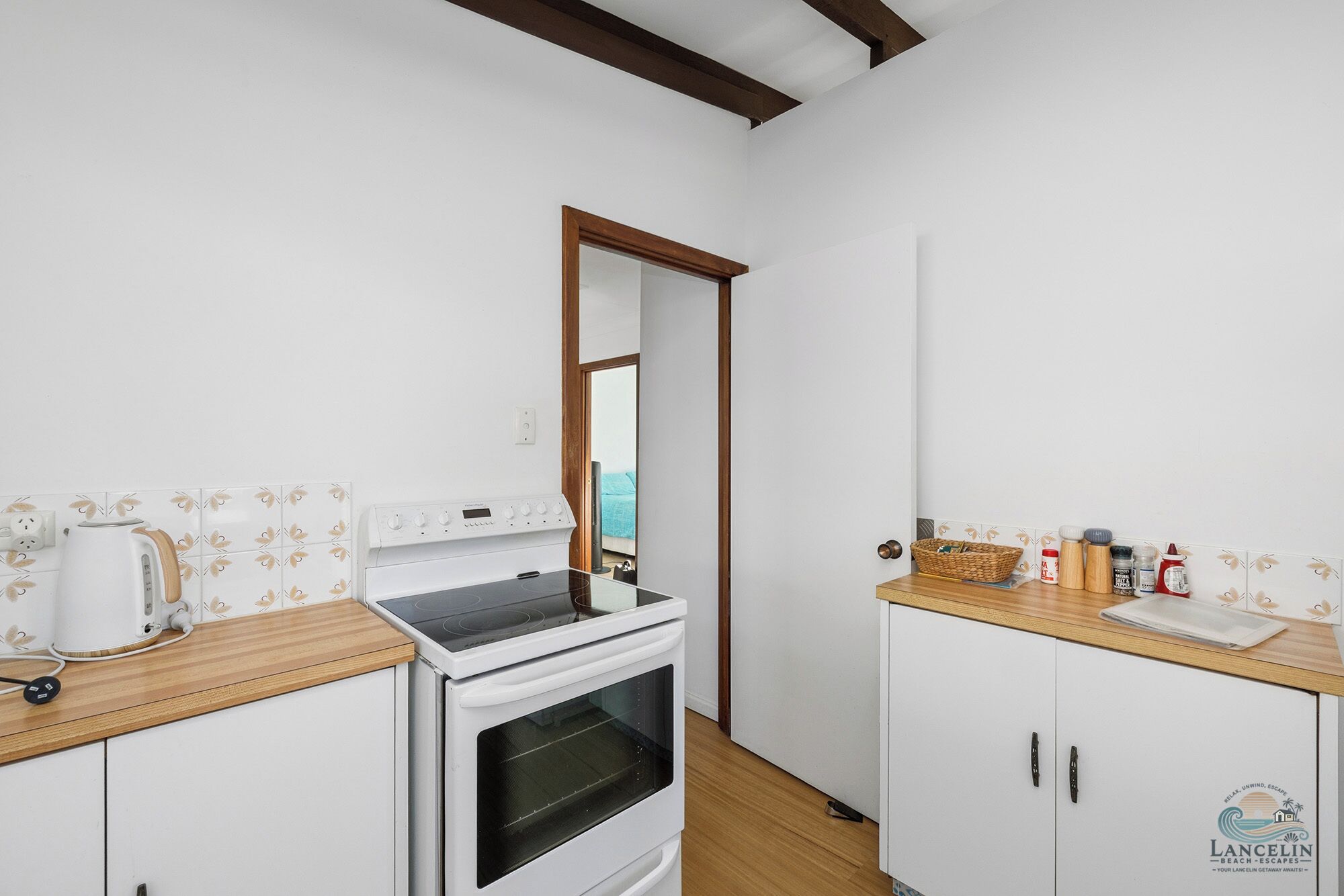 A compact kitchen with a stove, oven, and a kettle on the countertop.