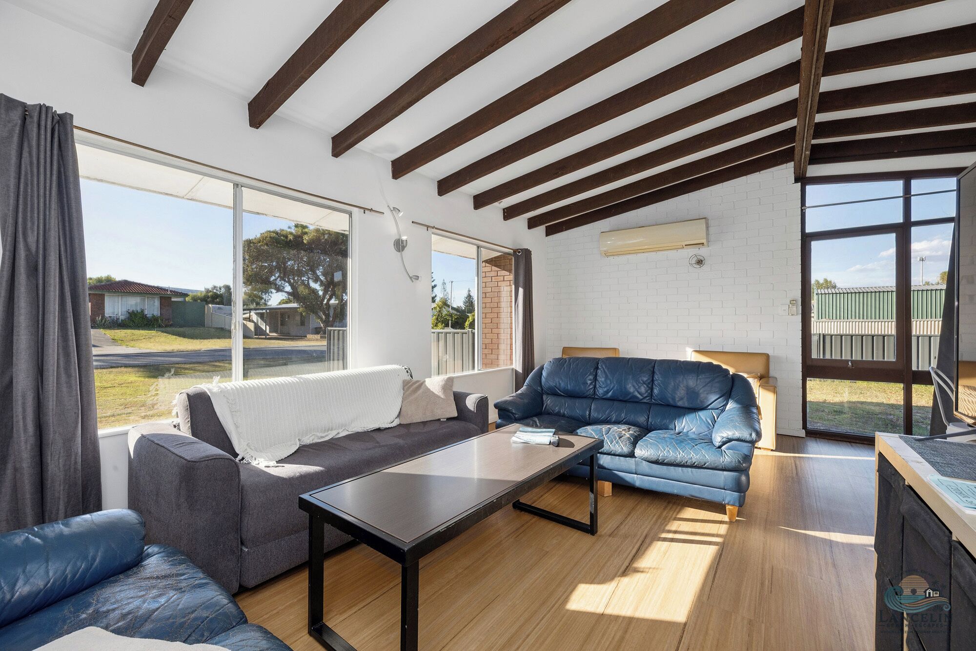 A spacious living area with a large window, a sofa, a coffee table, and a wooden floor.