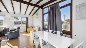Una habitación amplia con una mesa y sillas blancas, un sofá de cuero y vistas al exterior a través de grandes ventanales.