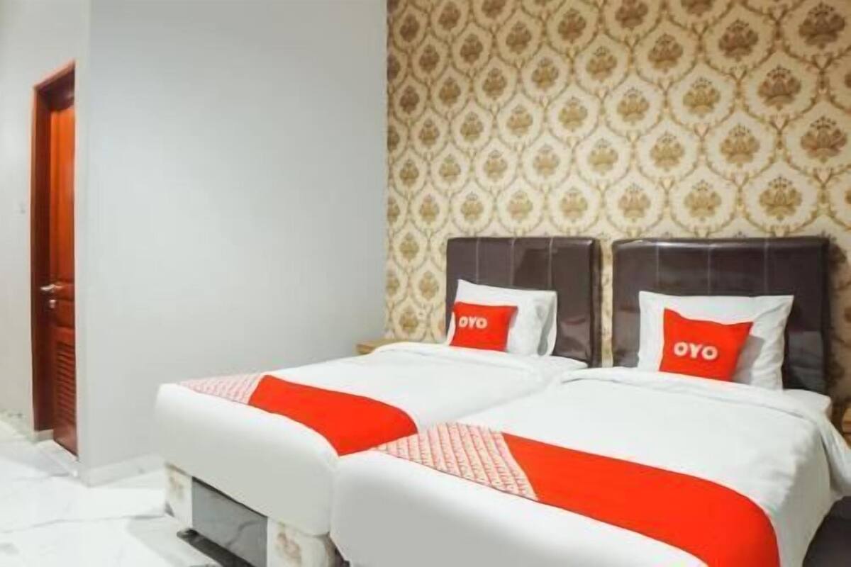 A hotel room with two beds, a patterned wallpaper, and a door.