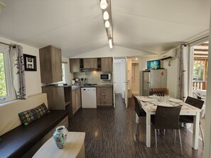 A compact kitchen with a microwave, stove, and sink, adjacent to a dining area with a table and chairs. - Welcome to Mobilandes Sanguinet in Nouvelle Aquitaine.  (Sanguinet)