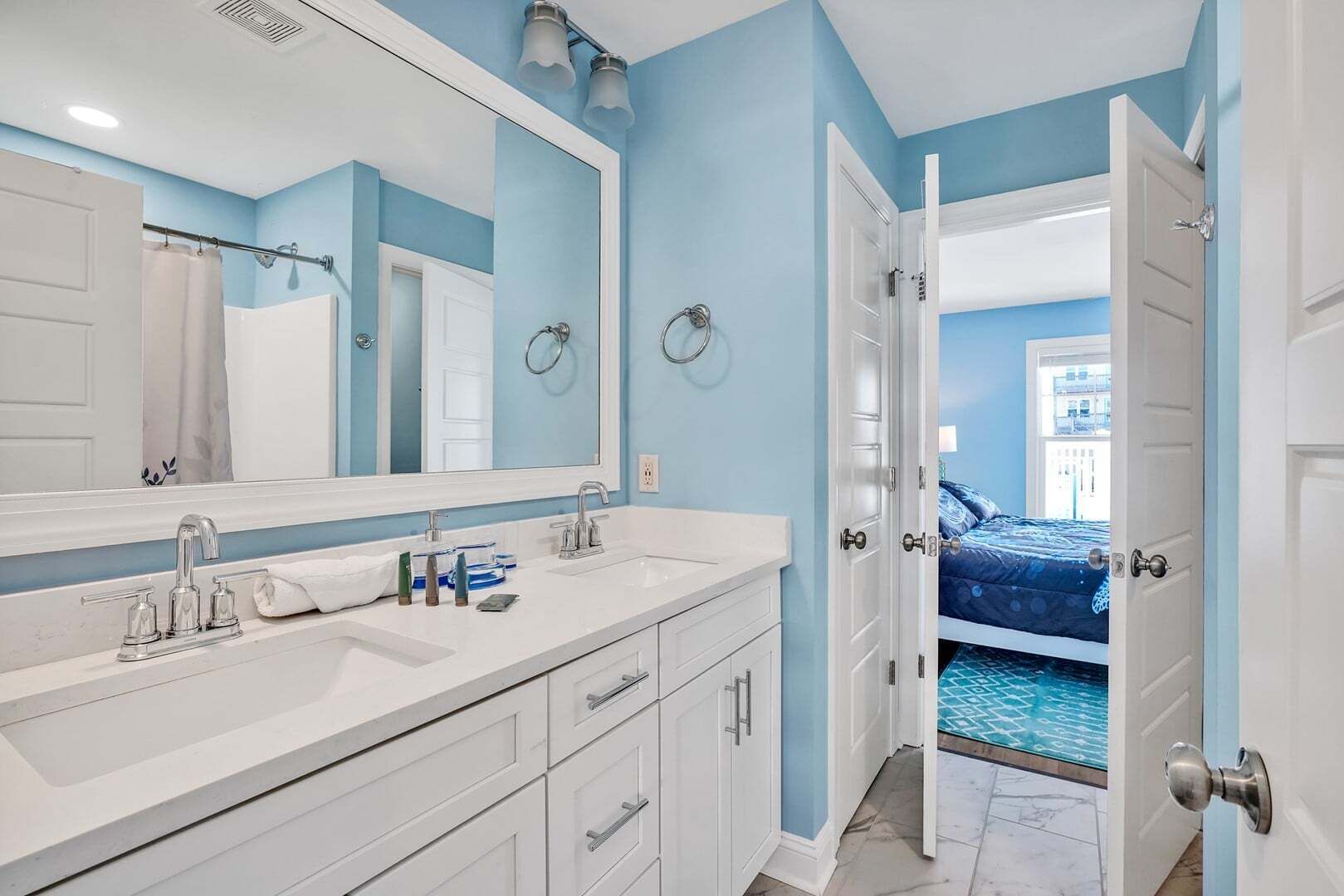 A bathroom with a large mirror, two sinks, and a shower curtain.