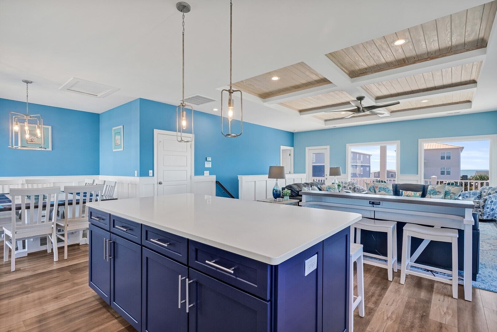 A modern kitchen with a central island, blue walls, and a dining area with white chairs.