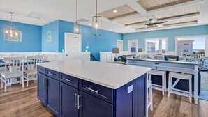 Une cuisine moderne avec un îlot central, des murs bleus et un coin repas avec des chaises blanches.