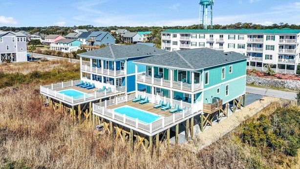 Une propriété de deux étages située en bord de mer, dotée d’une piscine, de chaises longues et offrant une vue sur l’océan.