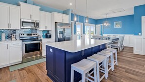 Une cuisine moderne avec des meubles blancs, des appareils en acier inoxydable, un mur d’accent bleu et un îlot central doté de tabourets de bar.