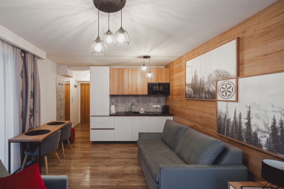Un salon moderne avec un canapé gris, une table à manger en bois avec des chaises, et un coin cuisine doté de meubles en bois et d’un four à micro-ondes.