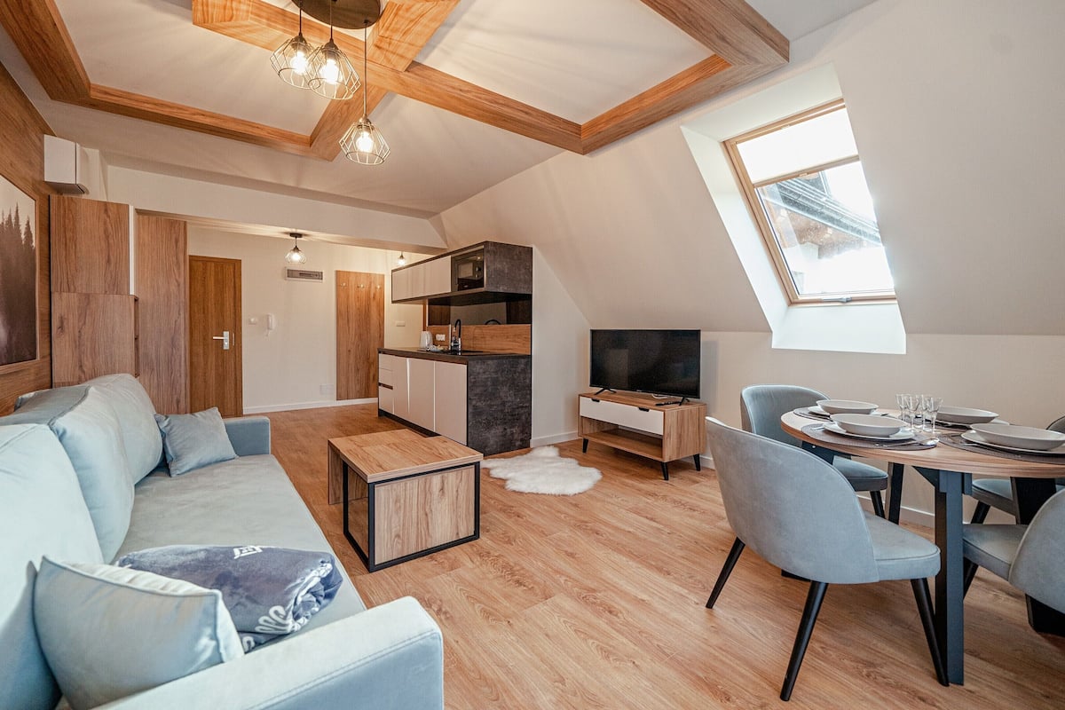 Un espace de vie moderne doté d’un plafond de style industriel, d’un coin repas avec une table ronde et d’un coin salon confortable avec un canapé.