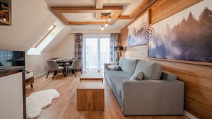 Una sala de estar moderna con techo de madera, un sofá gris, una mesa de comedor y un cuadro grande con temática forestal en la pared.