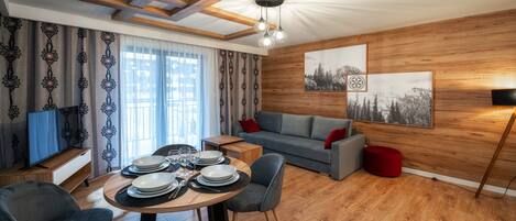 Een moderne woonkamer met een eethoek, houten wanden en een groot raam met gordijnen.