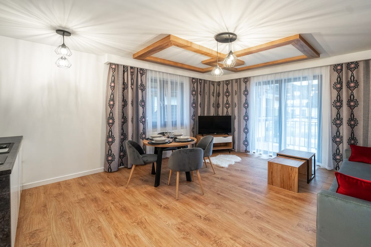 Un salon moderne comprenant un coin repas, un plancher en bois, un téléviseur et un canapé avec des coussins rouges.