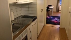 Cocina compacta con fregadero, estufa y alacenas, que da paso a un comedor con mesa y sillas.