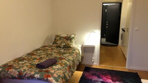 Un dormitorio pequeño y ordenado con una colcha de motivos florales, una alfombra con tema galáctico y una lámpara de noche.