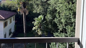 A balcony with a view of a garden, a palm tree, and a building with a tiled roof. - Tango House (Zandobbio)